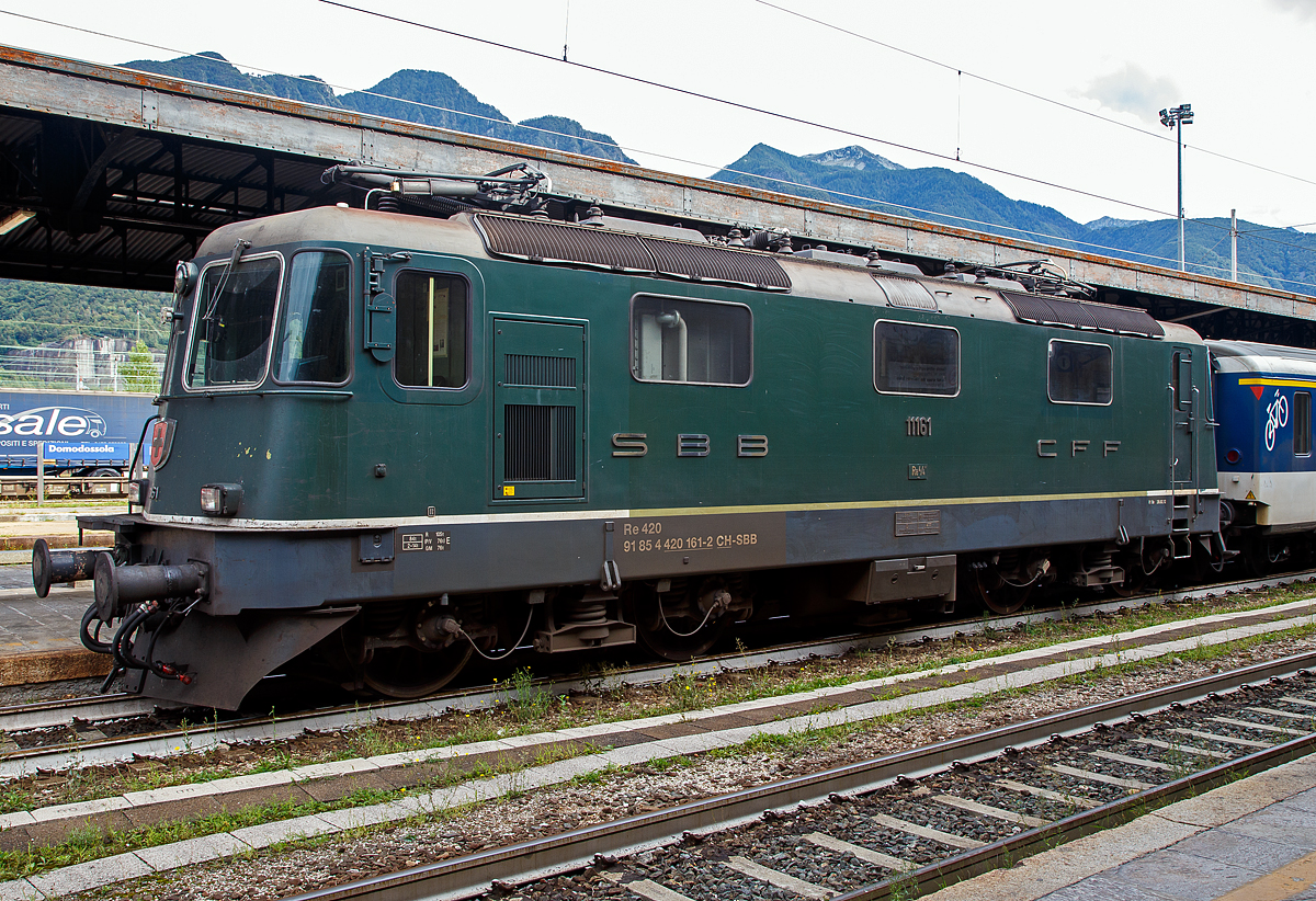 Die gr�ne SBB Re 4/4 II – 11161 (2. Serie) bzw. SBB 420 161-2 (91 85 4 420 161-2 CH-SBB) mit einem Einheitswagen I-Pendel (EW I), Regionalzug nach Brig, am 15.09.2019 im Bahnhof Domodossola.

Die Re 4/4II ist eine vierachsige, viermotorige Lokomotive auf zwei Drehgestellen. Die Rads�tze sind �ber Schraubenfedern am Drehgestellrahmen abgest�tzt. Das Drehgestell ist sekund�r mit Schraubenfedern (urspr�nglich Gummifedern) tief angeh�ngt am Lokomotivkasten abgest�tzt. Die Zugkraft�bertragung erfolgt �ber Tiefzugstangen von den Drehgestellen an den Lokomotivkasten.

Um einen besseren Kurveneinlauf des nachlaufenden Drehgestells zu erm�glichen, wurde zwischen den zwei Drehgestellen eine elastische Querkupplung eingebaut.

Diese Lokomotiven der zweiten Bauserie (11156–11349 und 11371–11397) haben zwei Einholmstromabnehmer und sind mit 15.410 mm (bei gleichem Drehgestellabstand) einen halben Meter l�nger als die Lokomotiven der 1. Serie. Die Stirnw�nde der Lokomotiven der 2. Serie sind etwas st�rker geneigt als diejenigen der 1. Serie.

TECHNISCHE DATEN (2.Serie):
Spurweite: 1.435 mm (Normalspur)
Achsfolge: Bo'Bo'
Hersteller: SLM / BBC / MFO / SAAS 
Dienstgewicht: 84 t (mit Klimaanlage)
L�nge �ber Puffer: 15.410mm 
Drehzapfenabstand:  7.900 mm
Achsabstand im Drehgestell: 2.800 mm
Treibraddurchmesser:  1.235 mm
Breite: 2.970 mm
H�he: 4.500 mm
Leistung: 4.700 kW (6.320 PS)
Stundenzugkraft: 167 kN
Anfahrzugkraft: 255 kN
H�chstgeschwindigkeit: 140 km/h
Stromsystem:  15 kV, 16,7 Hz AC