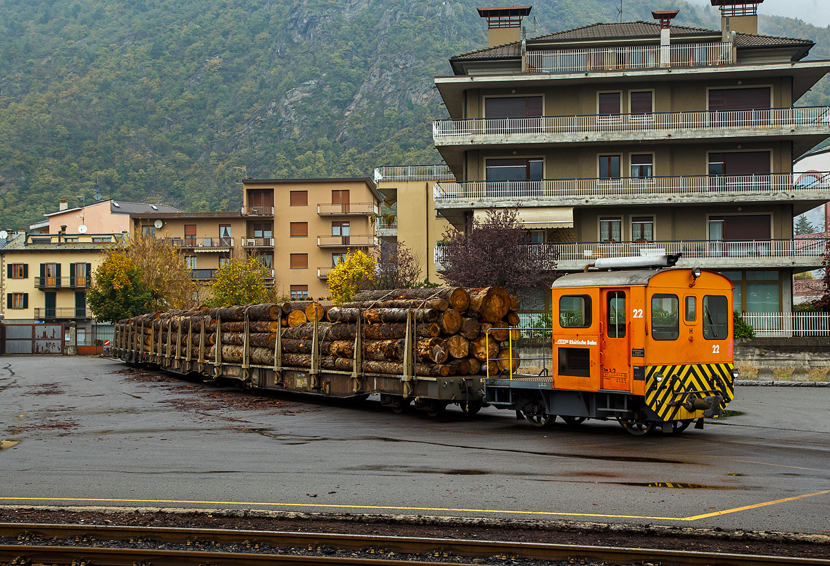 Die RhB Tm 2/2 22, ex RhB Tm 2/2 58, steht am 02.11.2019 mit drei angehangenen und mit Rundholz beladenen Flachwagen vom Typ “Sp-w“ der Serie 8271 – 8300 beim Bahnhof Tirano. 

Der Traktor vom Typ RACO 55 LA 4 wurde 1965 von RACO (Robert Aebi AG) unter der Fabriknummer 1717 gebaut. Im Jahr 1989 erfolgte die Remotorisierung mit einem Cummins Motor vom Typ 4BT 3.9 und die Umzeichnung in Tm 2/2 22.

Als Tm 2/2 werden diesel- oder benzinbetriebene Traktoren (Kleinlokomotiven) bezeichnet.
Die RhB besaß im Laufe der Jahre insgesamt 42 zweiachsige Traktoren mit Verbrennungsmotoren. Davon haben sechs eine Funkfernsteuerung und tragen deshalb die Bezeichnung Tmf 2/2. Die verbleibenden 36 Fahrzeuge teilen sich auf in 26 heute orange Rangierfahrzeuge und 10 heute gelbe Baudiensttraktoren. Insgesamt hatte die RhB 12 dieser baugleichen RACO 55 LA 4.

Zwischen 1957 und 1969 lieferte die Firma Robert Aebi (Raco) die dieselmechanischen Traktoren Tm 2/2 64–67, 62–63, 57–61 und schließlich noch Nummer 56. Die Nummerierung erfolgte vor den schon vorhandenen Tm 68 und 69. Basis für diese Fahrzeuge waren die Tm II der SBB. Der mechanische Aufbau wurde von RACO entwickelt und gebaut, der Dieselmotor war von Saurer-SLM. Die Kraftübertragung vom Motor auf die Achsen erfolgte mittels Kettenantrieb, dadurch sind diese Traktoren nur für den leichten Verschubdienst an Bahnhöfen geeignet. Bei einem Umbau in den Jahren 1989-90 wurden die Motoren von SLM durch solche von Cummins ausgetauscht, dabei wurden die Nummern auf 15 bis 26 geändert und die Traktoren dabei in die Ablieferungsreihenfolge gebracht. Die ursprünglich rotbraun, heute orange lackierten Fahrzeuge sind 5,06 m lang und 9 t schwer. Sie bestreiten den Rangierdienst auf Stationen mit kleinem bis mittlerem Güteraufkommen, wobei die meisten der 12 Traktoren ihrer jeweiligen «Heimatstation» fest zugeteilt sind.

TECHNISCHE DATEN:
Spurweite: 1.000 mm
Achsfolge: B
Länge über Puffer: 5.060 mm
Breite: 2.640 mm
Leergewicht: 9 t
Ladegewicht: 2 t
Höchstgeschwindigkeit: 30 km/h (55 km/h Schleppfahrt)
Motorbauart: 4-Zylinder-Dieselmotor
Motortyp: ab 1989/90 Cummins 4BT 3.9 (ursprünglich Saurer-SLM 4 VD 11)
Motorleistung: 62 kW (ursprünglich 44 kW)
Anfahrzugkraft: 30 kN (ursprünglich 25 kN)
Stundenzugkraft: 15 kN bei 10 km/h
Leistungsübertragung: Rollenkette

Die offenen, vierachsigen RhB Flachwagen mit Rungen vom Typ Sp-w der Serie 8271 – 8300 sind die Allrounder der Rhätischen Bahn schlechthin und werden vorwiegend für den Transport von Rundholz eingesetzt. An jeder Längsseite besitzen sie sechs Steckrungen.

TECHNISCHE DATEN vom Typ Sp-w (8271 bis 8300) :
Typenbezeichnung:  Sp-w
Wagennummern:  8271 bis 8300
Baujahr: 1979
Spurweite: 1.000 mm
Länge über Puffer: 16.540 mm 
Drehzapfenabstand: 11.000 mm 
Achsabstand im Drehgestell: 1.400 mm
Laufraddurchmesser: 750 mm (neu)
Breite über Alles: 2.700 mm
Ladelänge: 15.500 mm
Ladebreite:  2.310 mm
Rungenhöhe: 1.050 mm
Ladefläche: 34 m²
Eigengewicht:  ca. 15.600 kg
Ladegewicht:  33 Tonnen
Höhe ab Schienenoberkante: 965 mm