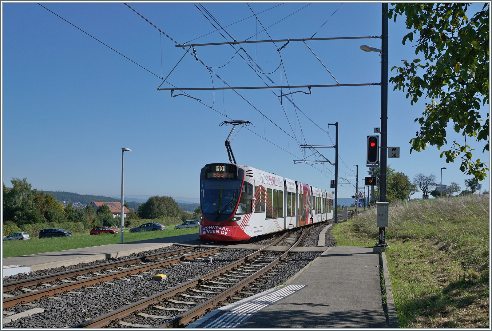 Aus der Grossstadt aufs Land - mit der BLT: Von Basel bzw. wohl Dornach kommend erreicht ein BLT Zug der Linie 10 das im Elsass gelegene Leymen und wird nach der Kreuzung mit dem Gegenzug nach Rodersdorf im Kanton Solothurn weiterfahren, oder anders ausgedrückt - eine Ban drei Kantone, zwei Länder...

Noch ein kleines Detail zum Signal rechts im Bild: Ein kleines  G  macht darauf aufmerksam, dass die Strecke durch den  G egenzug belegt ist.

26. Sept. 2023